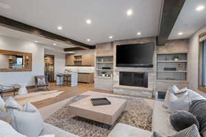 Living room featuring beamed ceiling, recessed lighting, a fireplace, light wood-style floors, and built in shelves