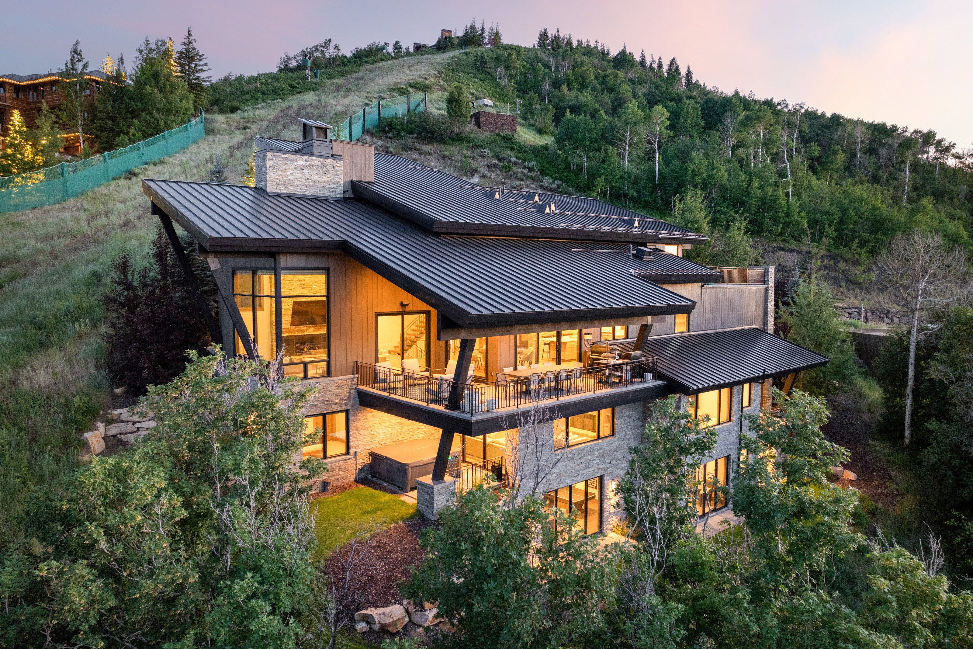 Back of house with a standing seam roof, stone siding, a metal roof, a chimney, and a balcony
