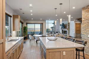 Kitchen with light stone counters, light brown cabinetry, hanging light fixtures, and recessed lighting
