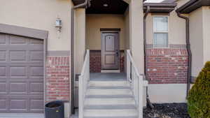 View of exterior entry featuring brick siding, stucco siding, and a garage