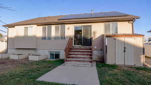 Back of property with entry steps, solar panels, a lawn, and a shed