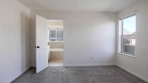 Unfurnished bedroom with carpet flooring, ensuite bathroom, and multiple windows