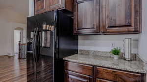Kitchen featuring black fridge with ice dispenser, light stone counters, dark brown cabinets, arched walkways, and dark wood-type flooring