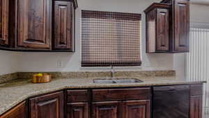 Kitchen with dark brown cabinets, dishwasher, and light stone countertops