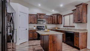 Kitchen featuring black appliances, dark brown cabinets, a kitchen island, light wood-style floors, and lofted ceiling