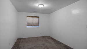 Carpeted empty room featuring a textured ceiling and a textured wall