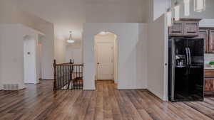 Kitchen with black refrigerator with ice dispenser, decorative light fixtures, light wood finished floors, and arched walkways
