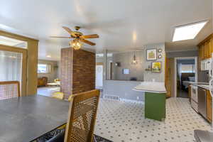 Kitchen featuring light countertops, light floors, stainless steel appliances, decorative light fixtures, and brown cabinets