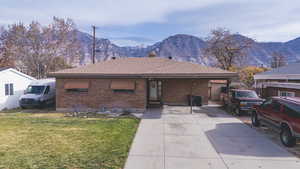 Ranch-style home with roof with shingles, brick siding, a mountain view, a front lawn, and driveway