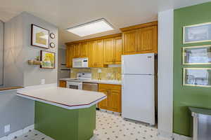 Kitchen featuring white appliances, light floors, light countertops, brown cabinetry, and tasteful backsplash