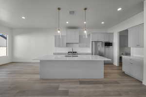 Kitchen featuring tasteful backsplash, decorative light fixtures, light wood-type flooring, a center island with sink, and stainless steel appliances