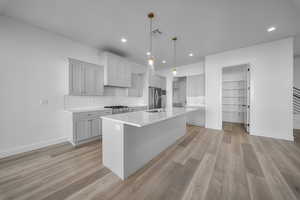 Kitchen with pendant lighting, a center island with sink, tasteful backsplash, light wood-type flooring, and recessed lighting