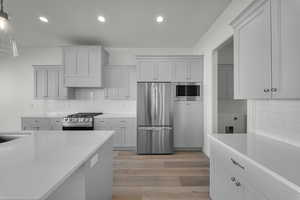 Kitchen with appliances with stainless steel finishes, backsplash, light wood-style floors, decorative light fixtures, and recessed lighting