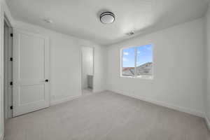 Unfurnished bedroom featuring light carpet, connected bathroom, and a textured ceiling