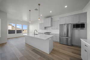Kitchen with stainless steel appliances, an island with sink, tasteful backsplash, dark wood-style flooring, and hanging light fixtures
