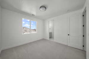 Unfurnished bedroom featuring light carpet, ensuite bath, and a textured ceiling