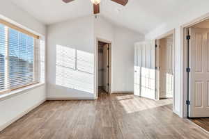 Unfurnished bedroom featuring a spacious closet, light wood-style floors, a ceiling fan, and lofted ceiling