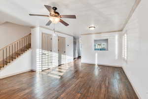 Unfurnished living room with ornamental molding, dark wood finished floors, stairway, and a ceiling fan