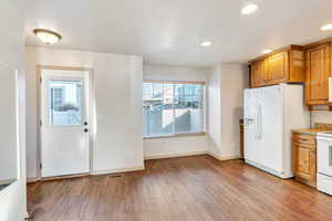 Kitchen featuring white appliances, light wood-type flooring, brown cabinetry, recessed lighting, and light stone countertops