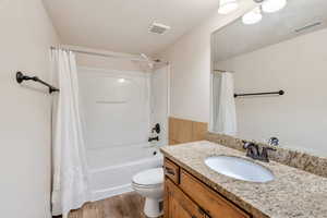 Full bathroom with vanity, shower / bathtub combination with curtain, light wood-style flooring, and a textured ceiling