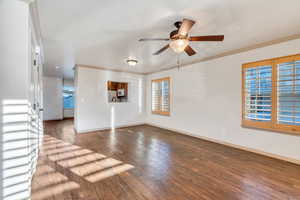 Unfurnished living room with dark wood finished floors, ceiling fan, and ornamental molding