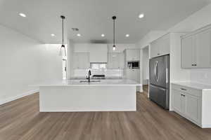 Kitchen featuring stainless steel appliances, light wood-style flooring, an island with sink, white cabinets, and decorative light fixtures