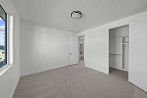 Unfurnished bedroom featuring light colored carpet and a walk in closet