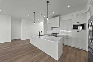 Kitchen featuring an island with sink, white cabinets, dark wood finished floors, stainless steel appliances, and pendant lighting