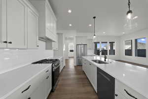 Kitchen with stainless steel appliances, dark wood finished floors, white cabinetry, recessed lighting, and hanging light fixtures