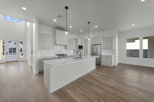 Kitchen featuring an island with sink, appliances with stainless steel finishes, pendant lighting, light wood-type flooring, and decorative backsplash