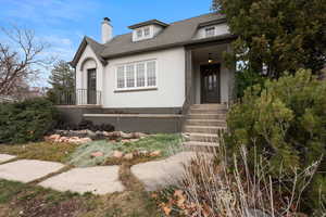 View of front facade with stucco siding, a shingled roof, and a chimney