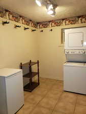 Laundry area featuring stacked washer and clothes dryer, light tile patterned flooring, and a textured ceiling