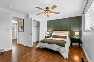 Bedroom with an accent wall, dark wood finished floors, ceiling fan, and a closet