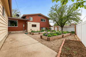 Rear view of property featuring a garden, a fenced backyard, brick siding, and a patio. Photo enhanced with A.I.