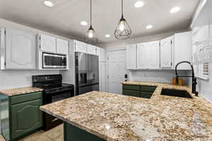Kitchen with green cabinets, stainless steel appliances, white cabinets, light stone countertops, and recessed lighting
