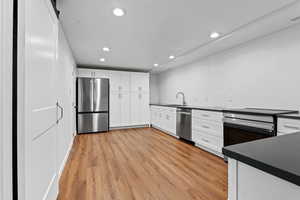 Kitchen featuring white cabinetry, recessed lighting, stainless steel appliances, light wood-type flooring, and a barn door