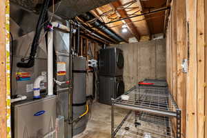 Utility room featuring water heater, heating unit, and stacked washing machine and dryer