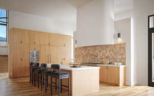 Kitchen featuring light brown cabinets, a breakfast bar area, modern cabinets, light wood-style floors, and a high ceiling