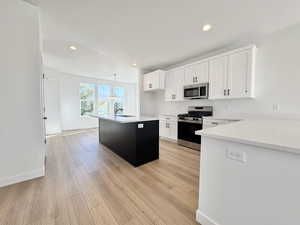 Kitchen with white cabinetry, stainless steel appliances, an island with sink, light stone countertops, and pendant lighting