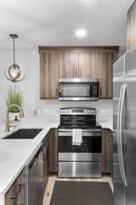 Kitchen with stainless steel appliances, a peninsula, hanging light fixtures, light stone countertops, and light wood-type flooring