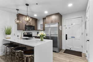 Kitchen featuring a breakfast bar, a peninsula, appliances with stainless steel finishes, decorative light fixtures, and light stone countertops