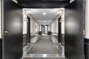 Hallway featuring recessed lighting, dark tile patterned floors, and wainscoting