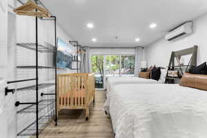 Bedroom featuring light wood-style floors, a wall mounted AC, and recessed lighting