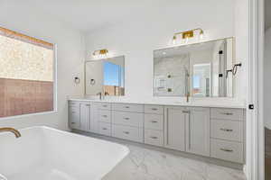 Bathroom featuring double vanity, a stall shower, a soaking tub, and light marble finish flooring