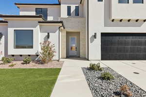 View of exterior entry with stone siding, stucco siding, a lawn, driveway, and a garage