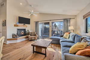 Living room with vaulted ceiling, hardwood / wood-style flooring, a glass covered fireplace, and a ceiling fan