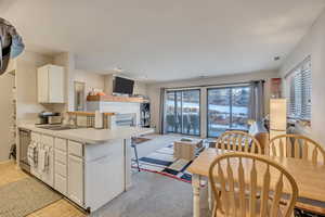 Kitchen with a peninsula, white cabinetry, a kitchen breakfast bar, light countertops, and light carpet