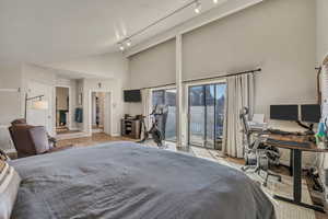 Bedroom featuring an office area, high vaulted ceiling, access to exterior, track lighting, and light wood-style flooring