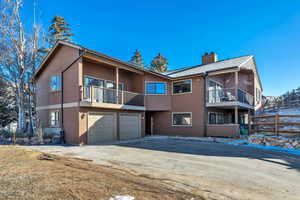 View of front of house featuring a balcony, a chimney, driveway, and a garage