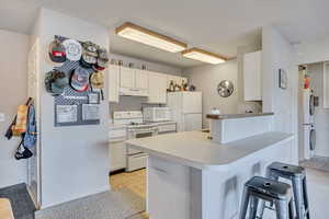 Kitchen with white cabinetry, white appliances, a kitchen bar, a peninsula, and light countertops